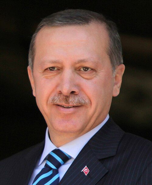 Portrait of Recep Tayyip Erdoğan, the President of Turkey, smiling and wearing a suit with a blue and white striped tie.